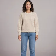 Woman in a cream knit sweater and straight jeans standing against a plain wall