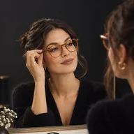 Woman at a mirror trying on round tortoiseshell glasses